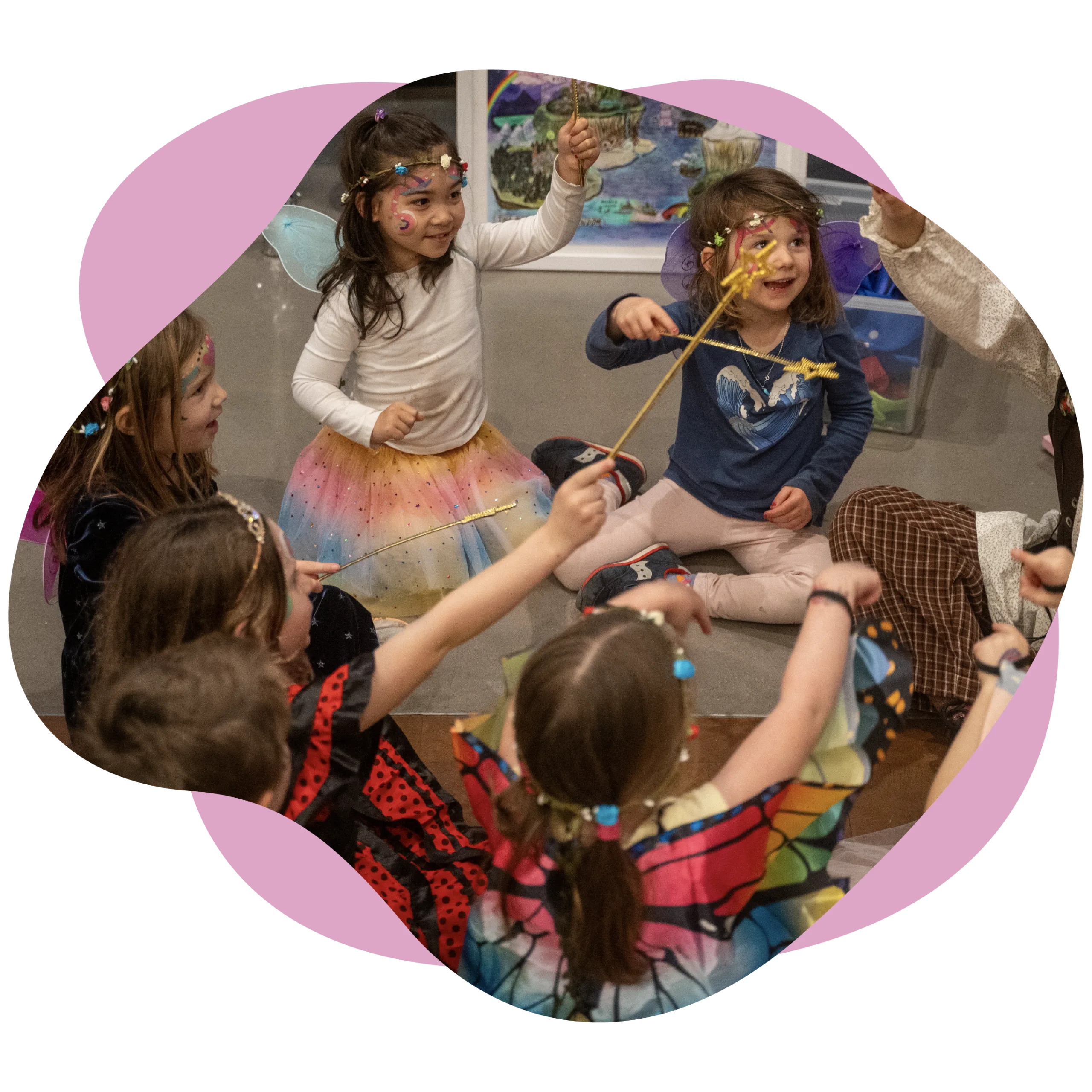 Children in costumes sit in a circle, smiling and holding colorful wands, as if ready for a whimsical production.