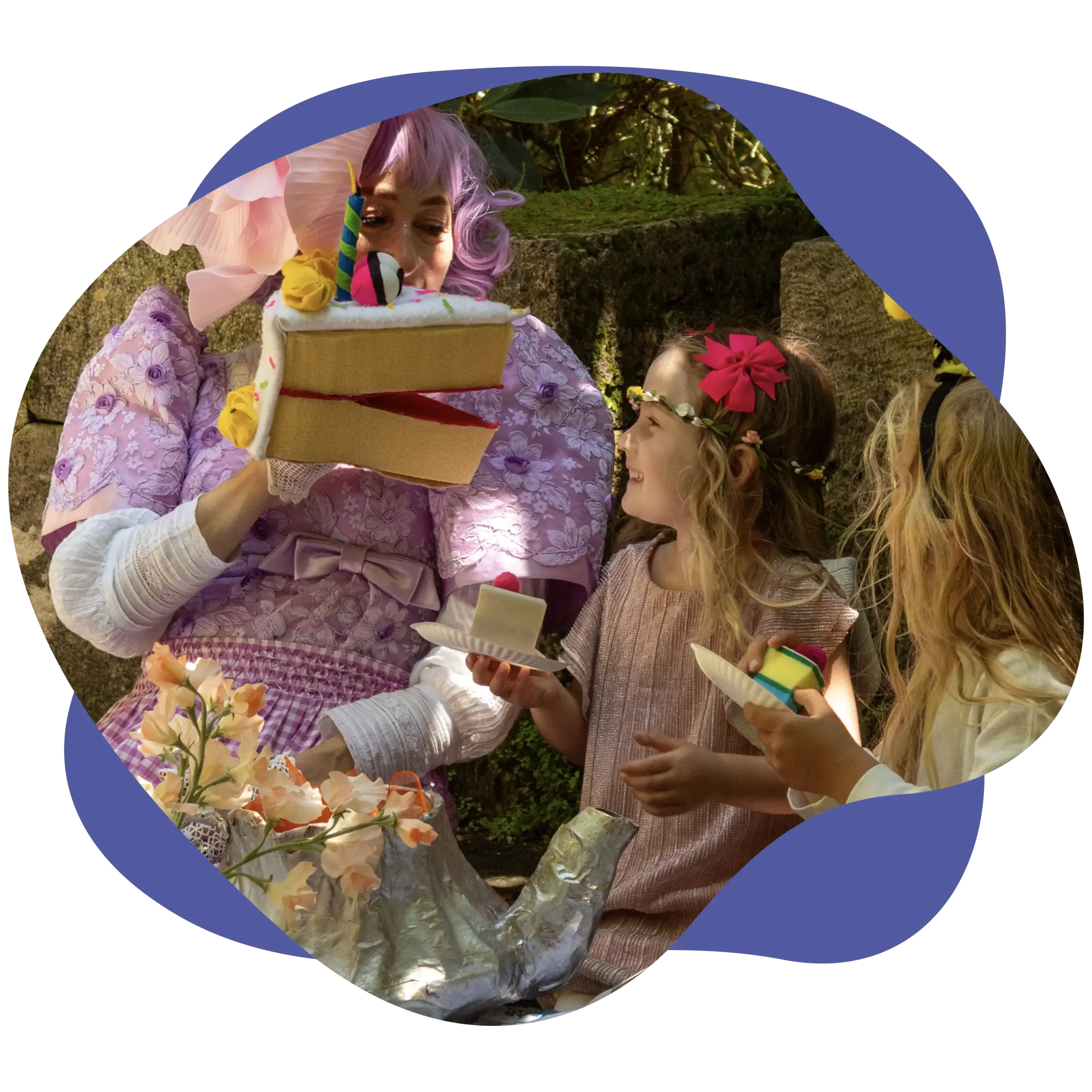 An adult in a purple costume holds a large puppet cake, entertaining two children at an outdoor birthday party with toy food.